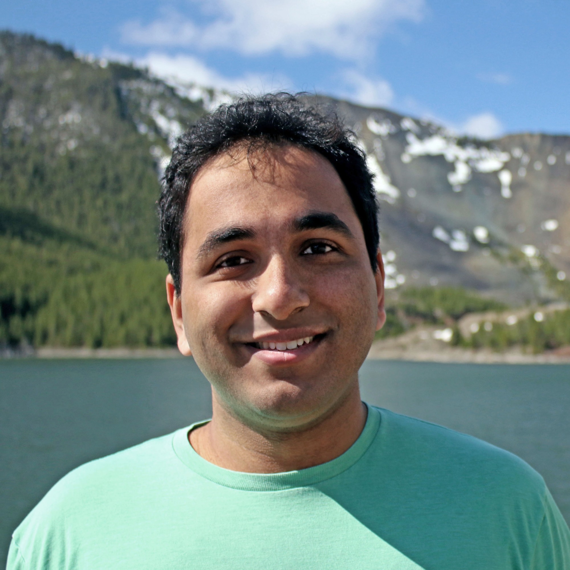 Anant Hariharan smiling in a green t-shirt with a snow dotted mountain and lake in the background