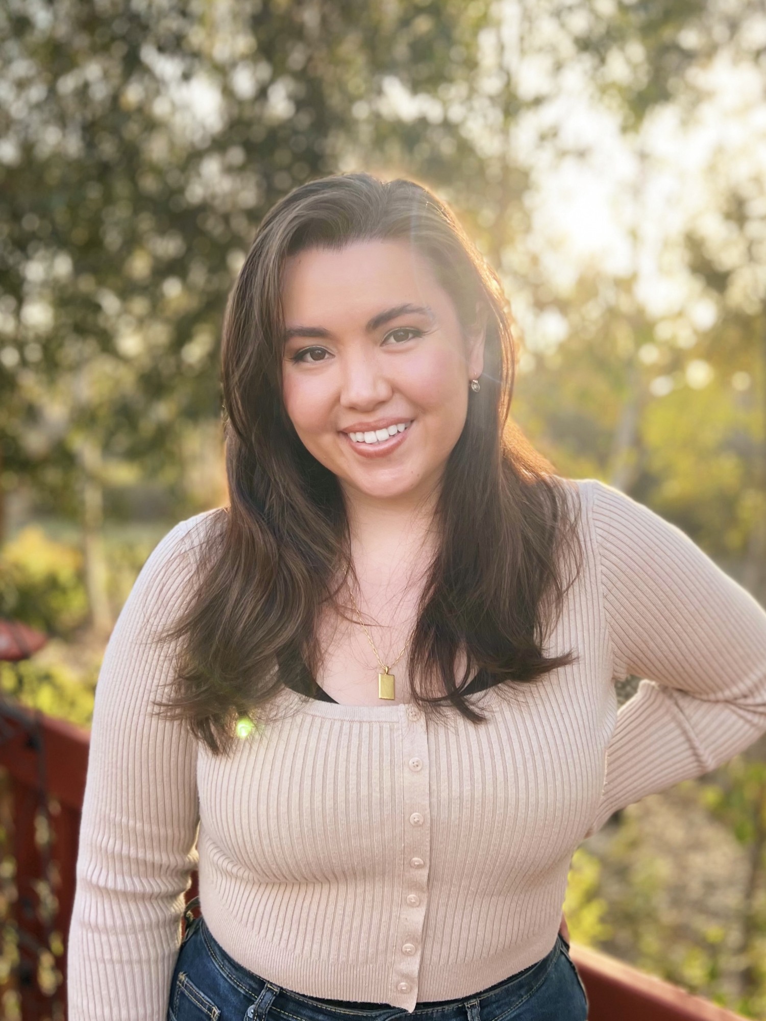 Headshot of Olivia Lafferty smiling, wearing a beige sweater with a background of trees with sun shining through.