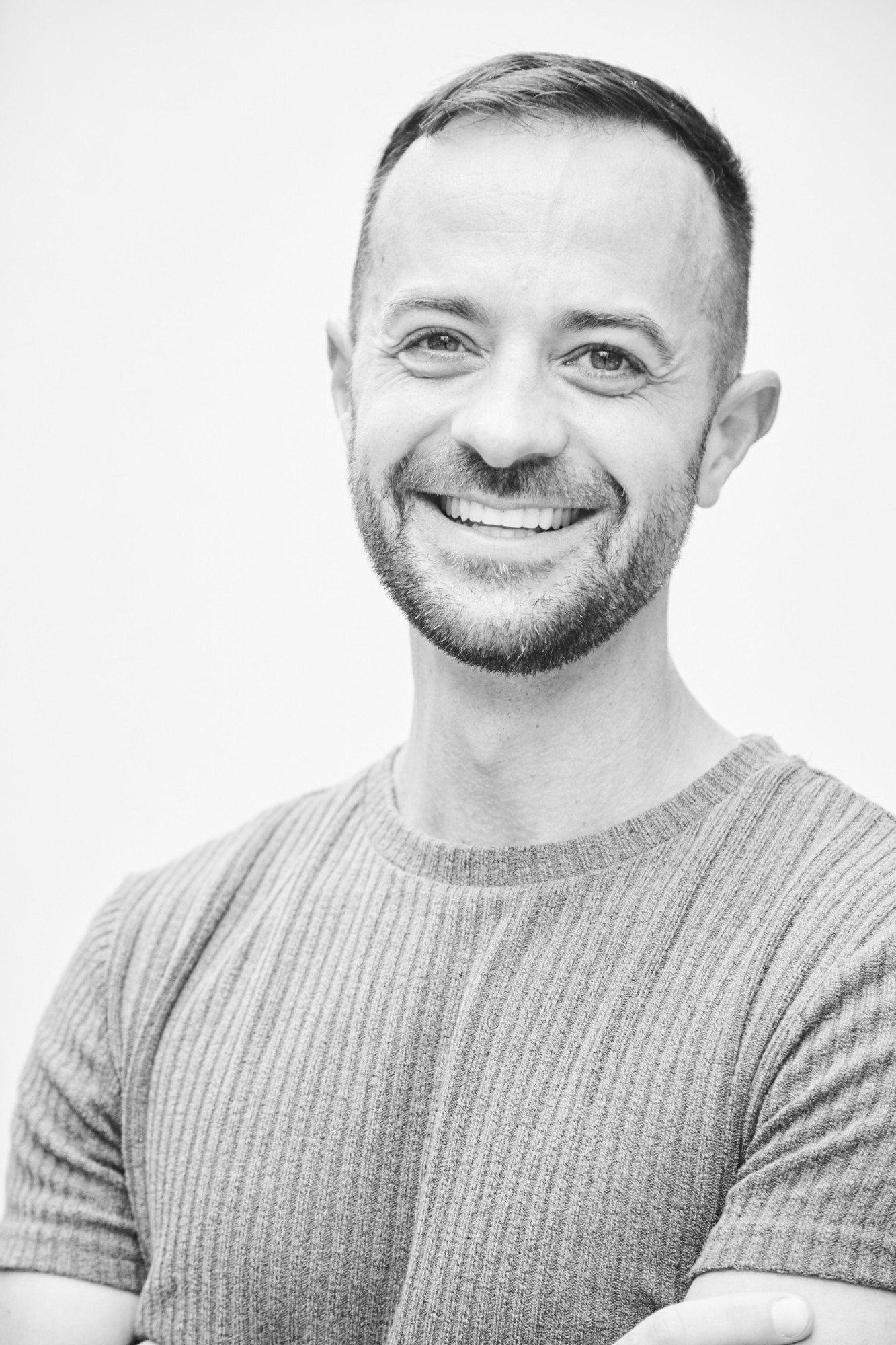 Black and white image of Wilfredo Giordano-Perez in a mid-grey short sleeve shirt, smiling. Light grey background.
