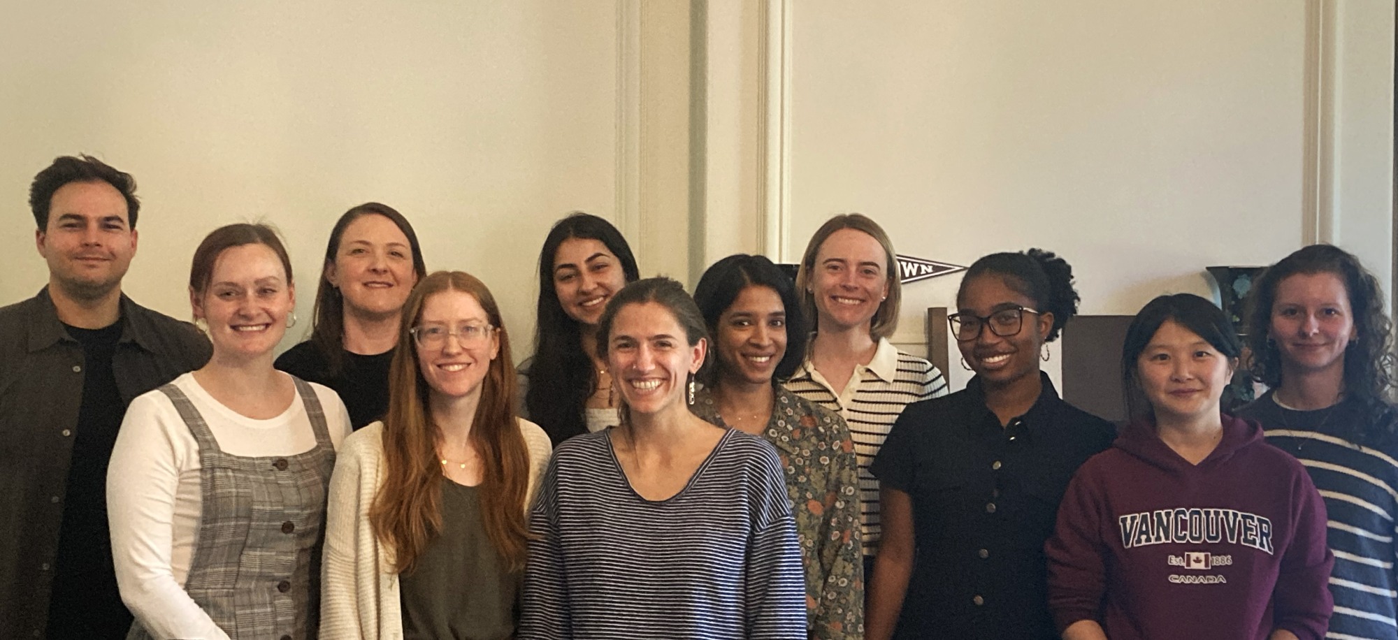  Group photo of eleven people standing and smiling in a brightly lit room. They are dressed in smart casual attire.
