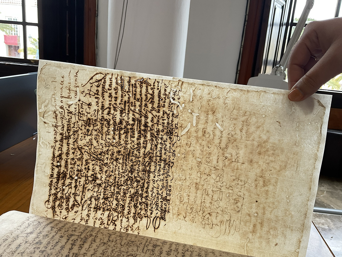 A close-up view of an aged, yellowed manuscript page filled with dense, dark cursive handwriting in ink, featuring natural discoloration, wear, and light stains along its edges.
