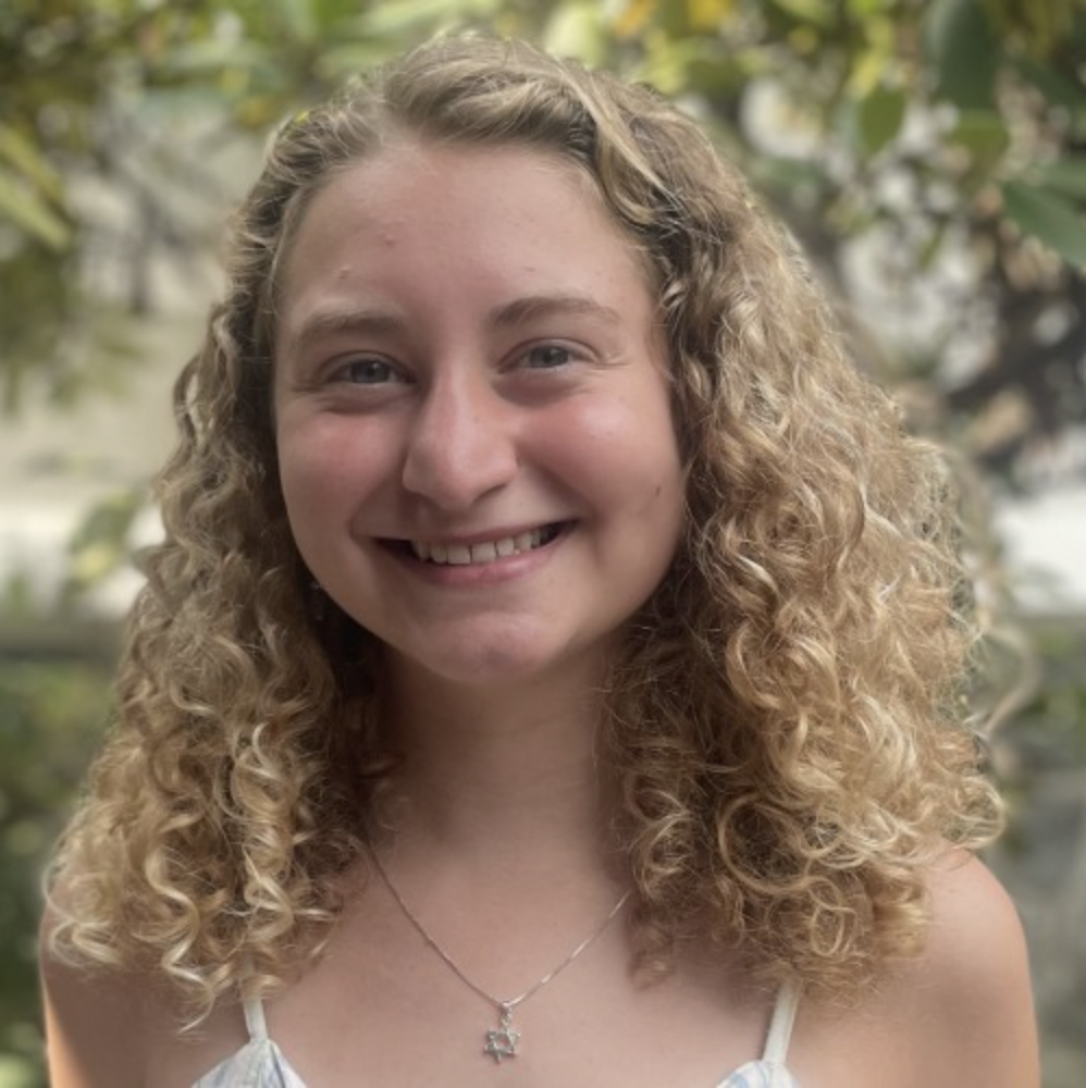 Ella Wilson, a Ph.D. candidate in mathematics, smiling and looking toward the camera with a tree in the background.
