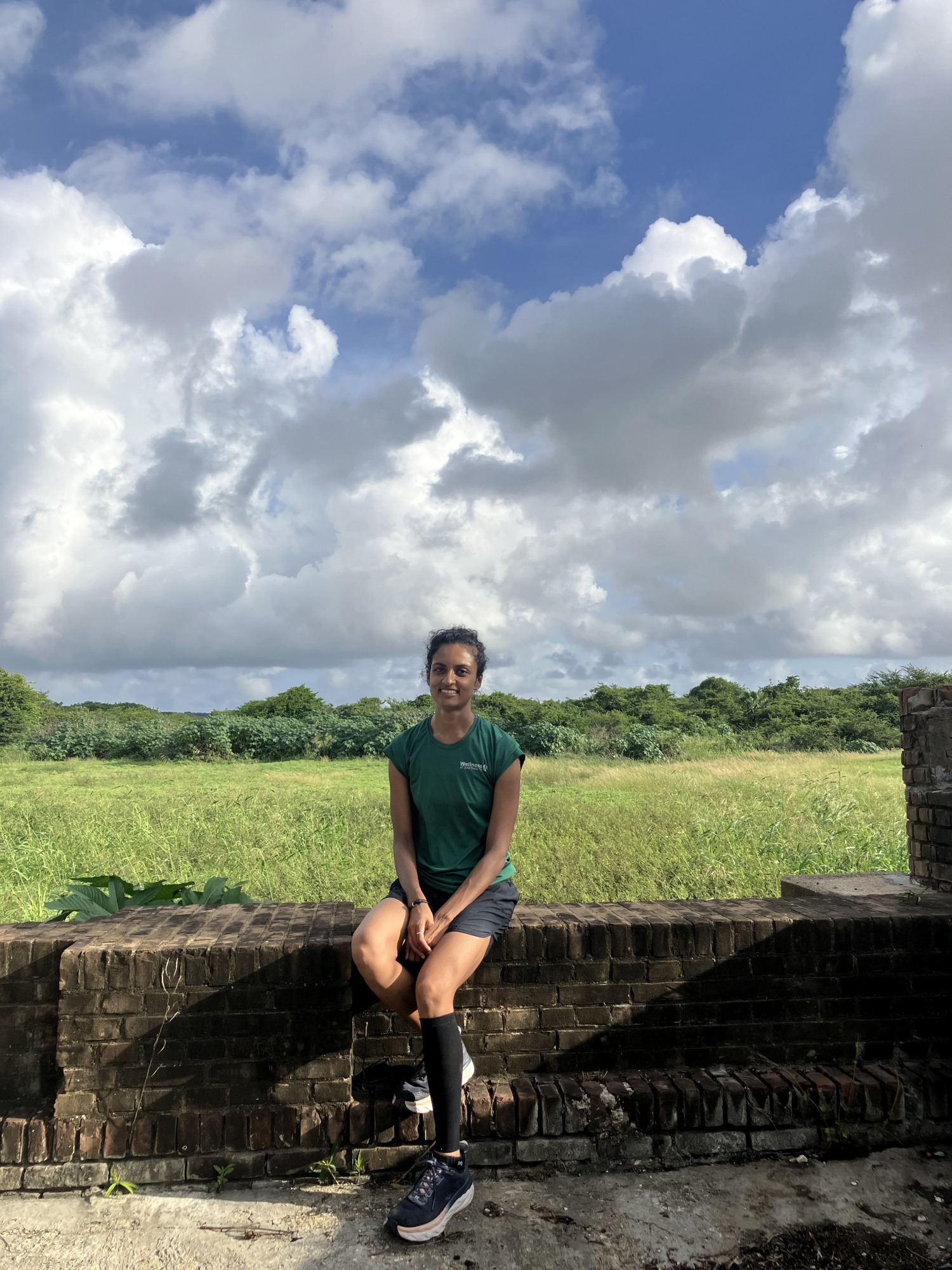 Archana Ramanujam sitting on a concrete wall with grass and blue sky behind