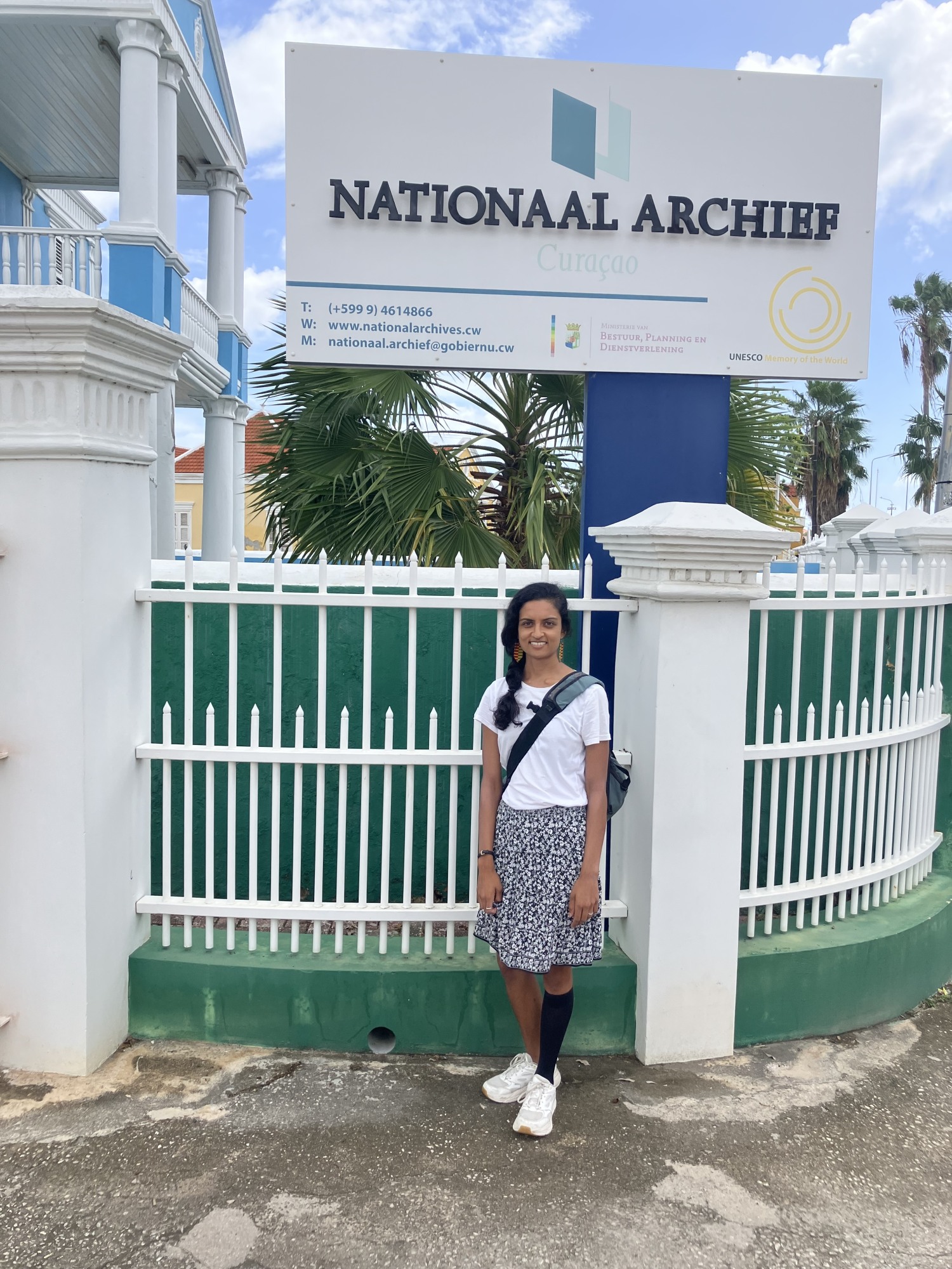 Archana Ramanujam in front of a white fence and sign for the Nationaal Archief