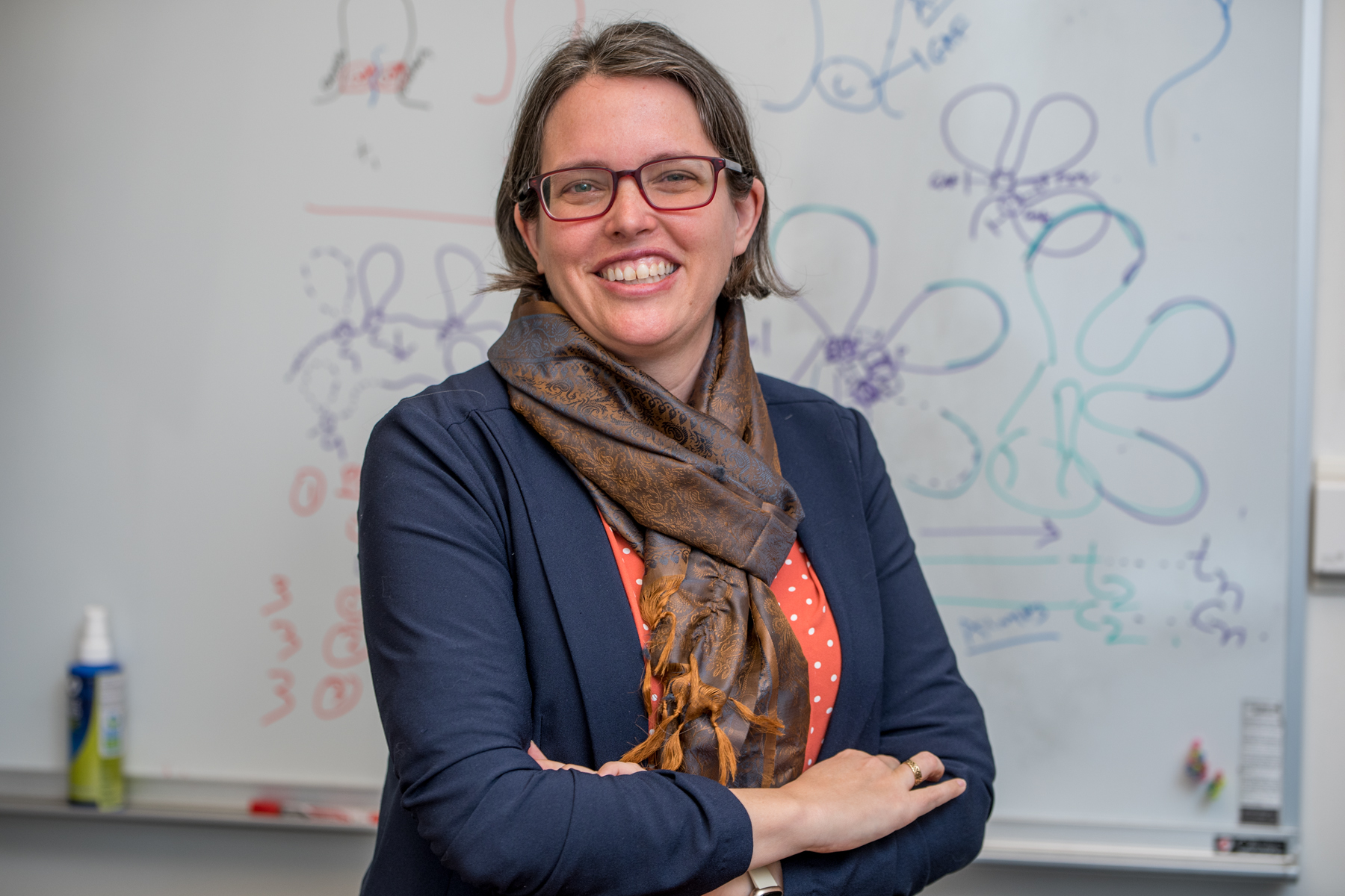 Erica Larschan, Professor of Molecular Biology, Cell Biology and Biochemistry, standing in front of a whiteboard with scientific diagrams.