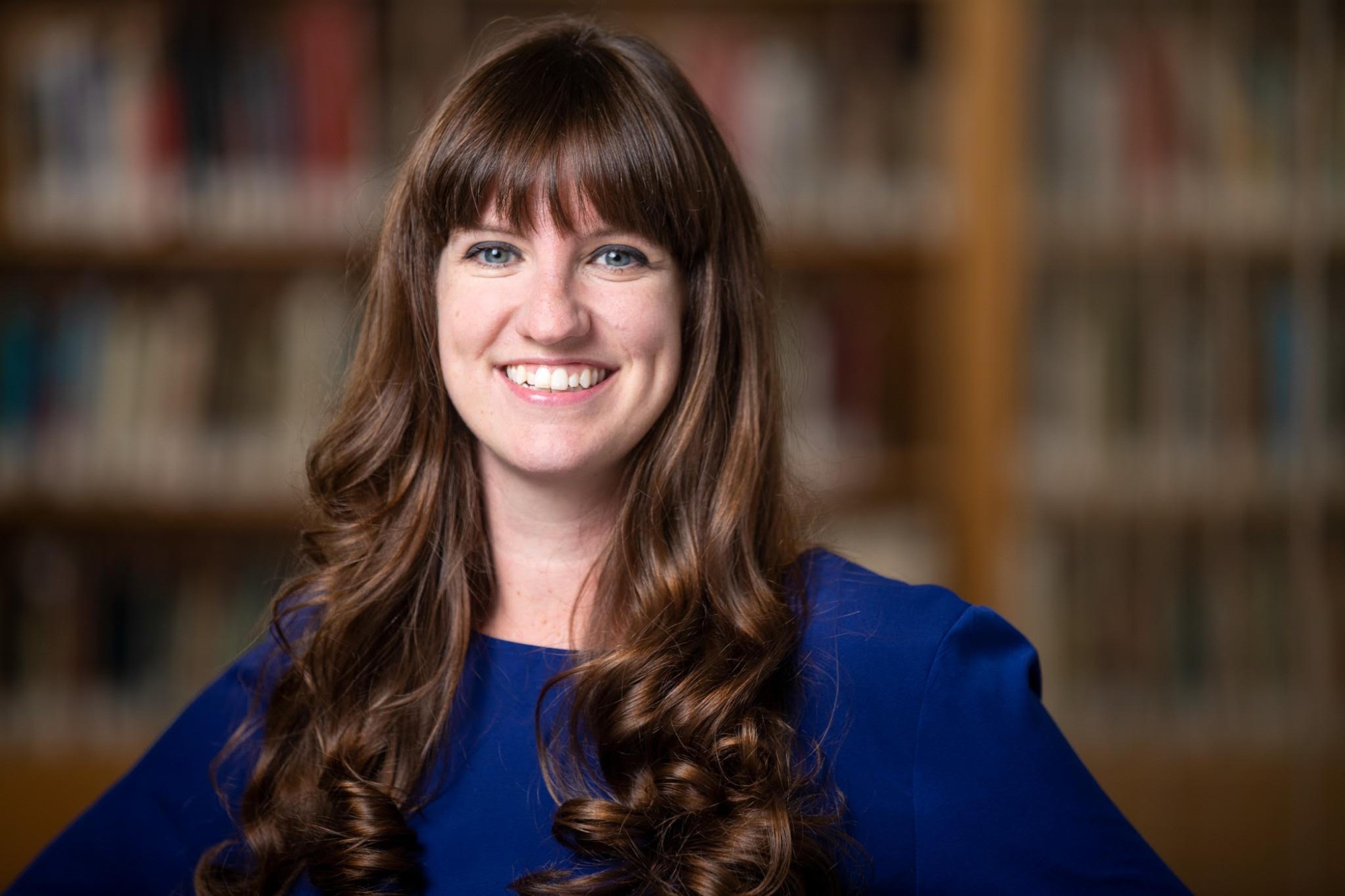 Candace Rice headshot in front of a bookshelf in a blue top