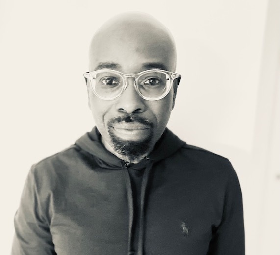 Headshot of Kevin Quashie in a black and white photo in a dark hooded shirt, wearing glasses.