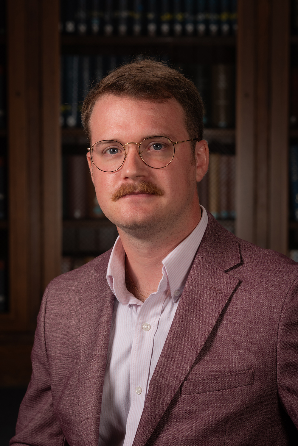 Michael Anzalone headshot in a dark jacket in front of a cabinet of books