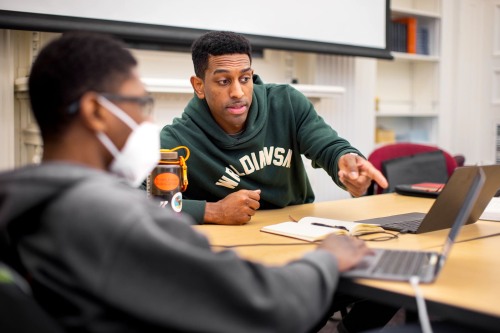 Two students collaborating at a table with laptops