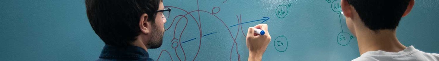 A man in glasses drawing on a blue dry-erase board while a student looks on.