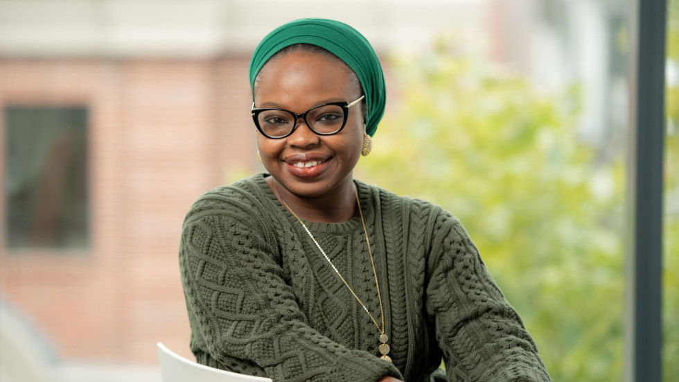  A woman wearing glasses, a green head covering, and a green knitted sweater smiles at the camera.